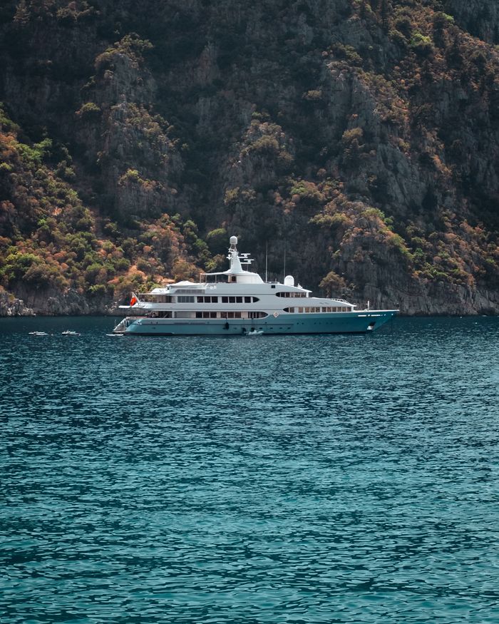 team-01 A luxury yacht sailing through clear blue waters against a rocky coastal backdrop.