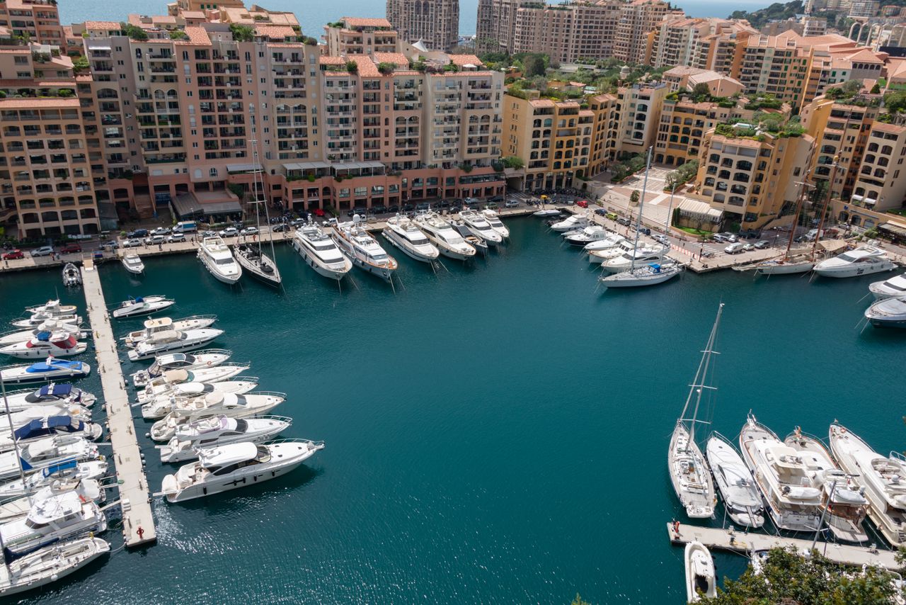 who-we-are Aerial view of luxury yachts moored at a marina in Monaco with buildings in the backdrop.