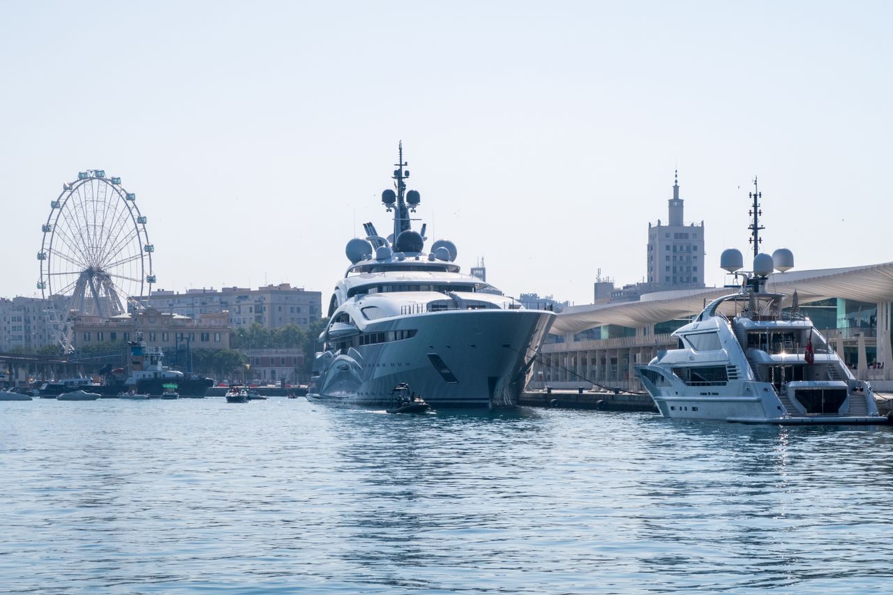 team-03 Majestic luxury yachts docked at a bustling city harbor with a ferris wheel and clear summer sky.