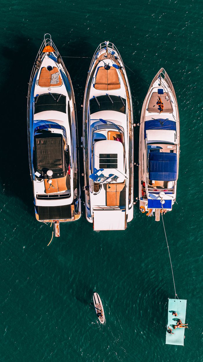 services-04 Aerial shot of three luxury yachts moored side by side in clear blue ocean, showcasing opulent leisure.